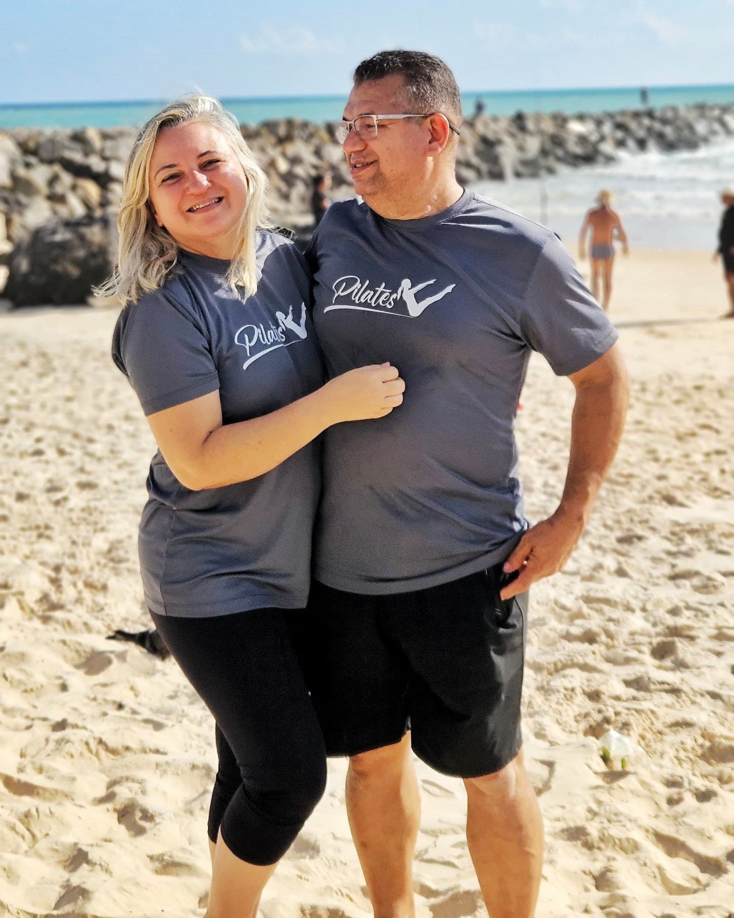 Casal na praia vestindo camisetas cinza personalizadas com a arte de um estúdio de pilates